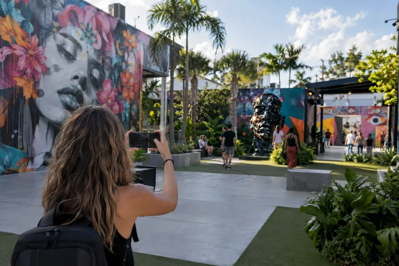 Patio ajardinado de Wynwood Walls con murales de arte urbano y una visitante fotografiándolos