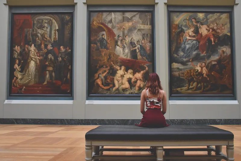 Visitante contempla pinturas en una galería de museo desde un banco